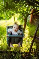 linda pequeño niña en el balancearse. bebé columpio en el árbol en el jardín. infantil jugando en el patio interior foto