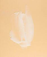 Smear of white cream for face and body on a brown background photo