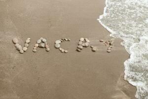 palabra Vacaciones escrito con Guijarro piedras en el playa con un ola foto