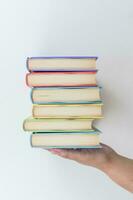 Female hand holding stacked books on white background. Study. Textbooks. photo