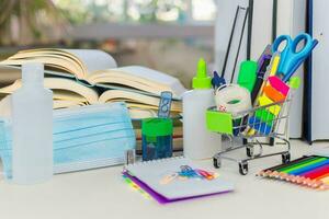 School supplies, protective mask, alcohol gel, books, on the desk. Back to school during a covid-19 pandemic. photo