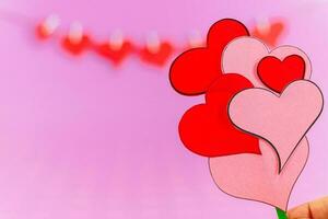 rojo amor corazones y hembra mano con ramo de flores de pequeño corazones en rosado antecedentes. foto