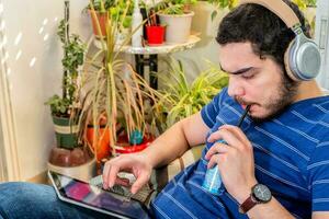 Young man in balcony with wireless headphones and digital tablet, drink soda. photo