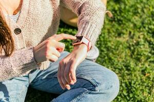 cerca arriba de mujer manos cheques el hora en inteligente reloj sentado en un parque foto