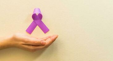 Woman hand holding purple ribbons on beige background. world cancer day. photo
