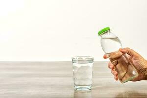 Female hand holding water bottle and glass on wooden table. photo