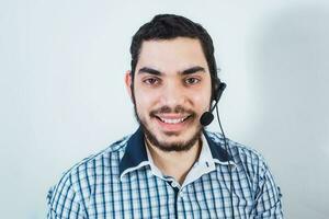 sonriente joven oficina trabajador vistiendo un auriculares y mirando a el cámara, hombre con el barba trabajando en el cliente Servicio Departamento foto