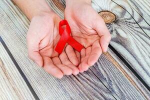 World Aids Day, AID red ribbon in hands on a wooden background photo