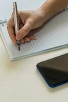 Close up of female hands writing in spiral notepad placed on white desktop, using an ink fountain pen. photo