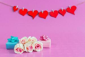 Red love hearts with small gifts and roses on pink background. photo
