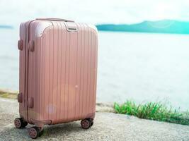 One pastel pink suitcase Laid out in the background is a blurred view of the sea on a sunny day. suitable for going on vacation photo