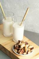 Vegan milk. Two glasses with brazil nut milk, bamboo drinking straws, plate of nuts on wooden board photo