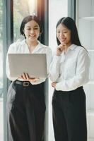 Two office workers talking with experienced colleague while using laptop computer in office, Colleagues discuss business photo