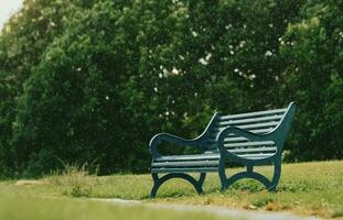 Bench in the local park with blurry rain falling on Spring forest background, Blue Metal stylish Bench in the Park with Green Lawn on Summer Background, Retro vintage tone photo