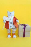 A soft toy cat stands near a gift box on a yellow background photo