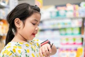 Cute Asian girl talks to her parents through a pink smartwatch in a department store.The smartwatch can be used to communicate between parents and children and can also find the child's location. photo