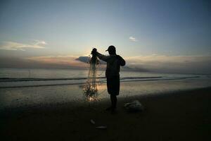 el belleza de el puesta de sol en el playa con el silueta de un pescador foto