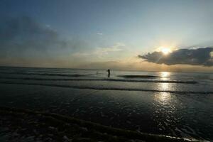 the beauty of the sunset on the beach with the silhouette of a fisherman photo