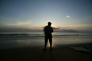 el belleza de el puesta de sol en el playa con el silueta de un pescador foto