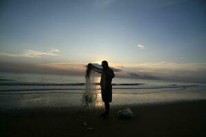 el belleza de el puesta de sol en el playa con el silueta de un pescador foto