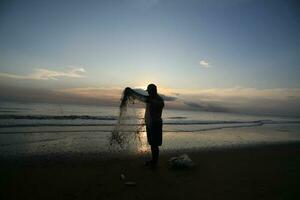el belleza de el puesta de sol en el playa con el silueta de un pescador foto