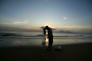 el belleza de el puesta de sol en el playa con el silueta de un pescador foto