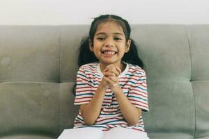 Little asian girl reading book on sofa in living room at home photo