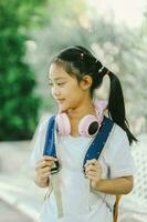 Portrait of cute little girl with backpack and headphones listening to music in the park. photo