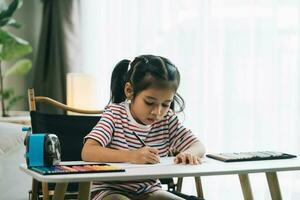 Little asian girl drawing with pencils in living room at home photo
