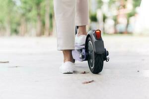 Close-up of woman legs in white sneakers riding electric scooter. photo