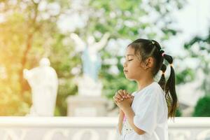 pequeño asiático niña Orando a Dios en el parque. religión concepto. foto