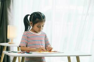 pequeño asiático niño niña dibujo con vistoso lápices de color a hogar foto