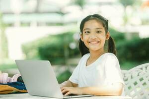 retrato de contento asiático niña utilizando ordenador portátil computadora a al aire libre jardín. foto
