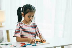 pequeño asiático niña jugando con vistoso arcilla de moldear en mesa a hogar foto