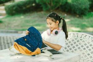 Little asian girl using laptop and listening to music in the park. photo