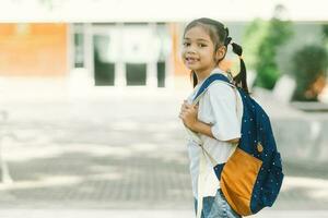 retrato de linda pequeño asiático Chica de escuela con mochila a colegio foto