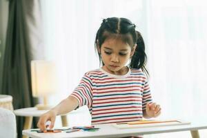 asiático pequeño niña dibujo con lápices de color en el vivo habitación a hogar foto