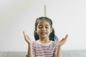 Little asian girl praying on the sofa in the living room. photo