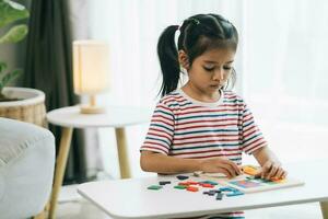 Little asian girl drawing with colorful pencils at table in living room photo