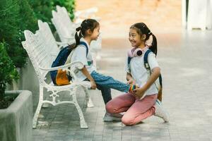 espalda a colegio concepto. dos pequeño muchachas sentado en el banco y sonriente foto