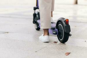 de cerca de mujer piernas montando eléctrico scooter en el ciudad foto