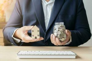 negocio hombre trabajando con ordenador portátil ahorros dinero tailandés moneda monedas en tarro para nuevo casa. salvar dinero a alquilar o comprar nuevo vivo lugar. foto