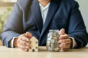 negocio hombre trabajando con ordenador portátil ahorros dinero tailandés moneda monedas en tarro para nuevo casa. salvar dinero a alquilar o comprar nuevo vivo lugar. foto