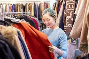 Stylish Asian woman is choosing the second hand sweater from the clothing shop for winter season fashion to keep warm at the new year and christmas holiday photo