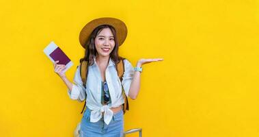 Pretty Asian woman passenger is holding passport with boarding pass for travel and summer vacation isolated on yellow background photo