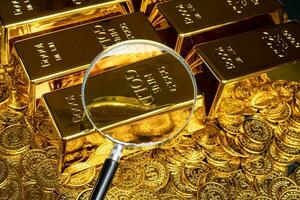 Magnifying glass with gold bar pile of gold coins under it photo