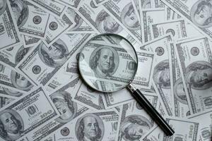 Magnifying glass on a pile of hundred us dollar money photo