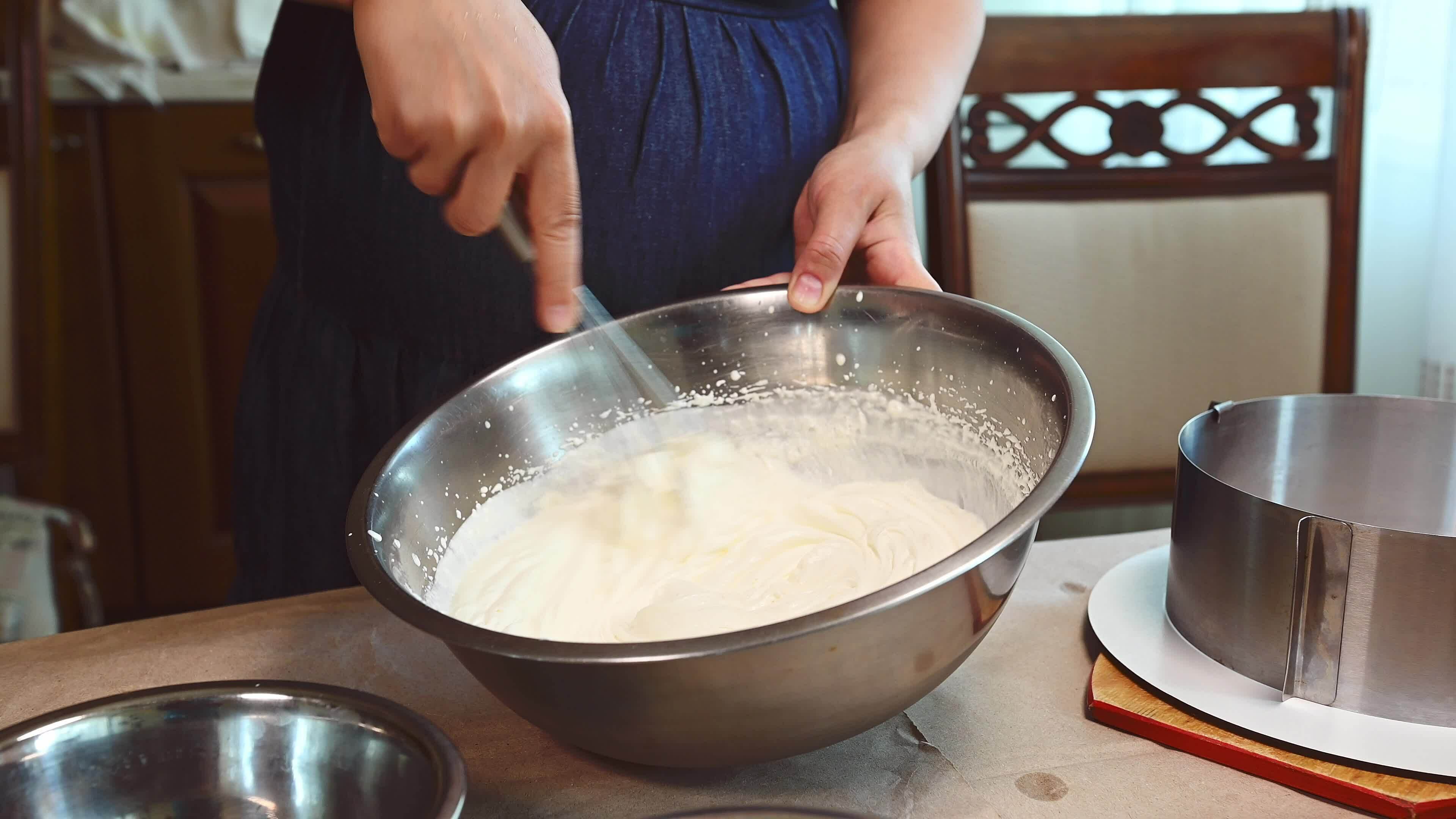 Closeup housewife whipping fresh cream by hand with a whisk to steady peaks, standing at the