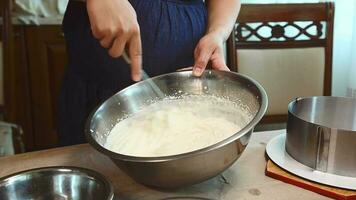 Close-up housewife whipping fresh cream by hand with a whisk to steady peaks, standing at the kitchen table at home video