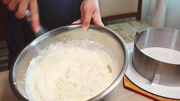 närbild av en bakverk kock använder sig av en vispa, spöstraff färsk grädde och blandning med pulveriserad socker i en metall skål. framställning en mousse kaka i de kök. konfektyr. bageri. matlagning. mat industri video